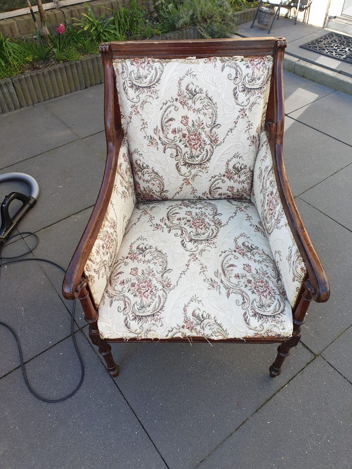 Antique armchair before restoration, with worn floral tapestry fabric